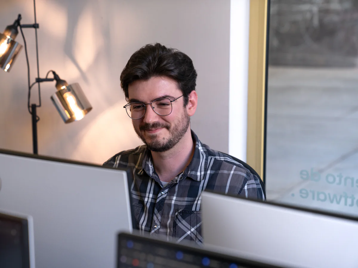 An AppX developer at their desk, monitors either side and code on screen