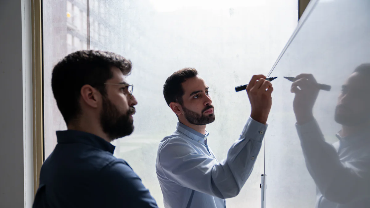 Two of the AppX team sketching at a whiteboard by the office window
